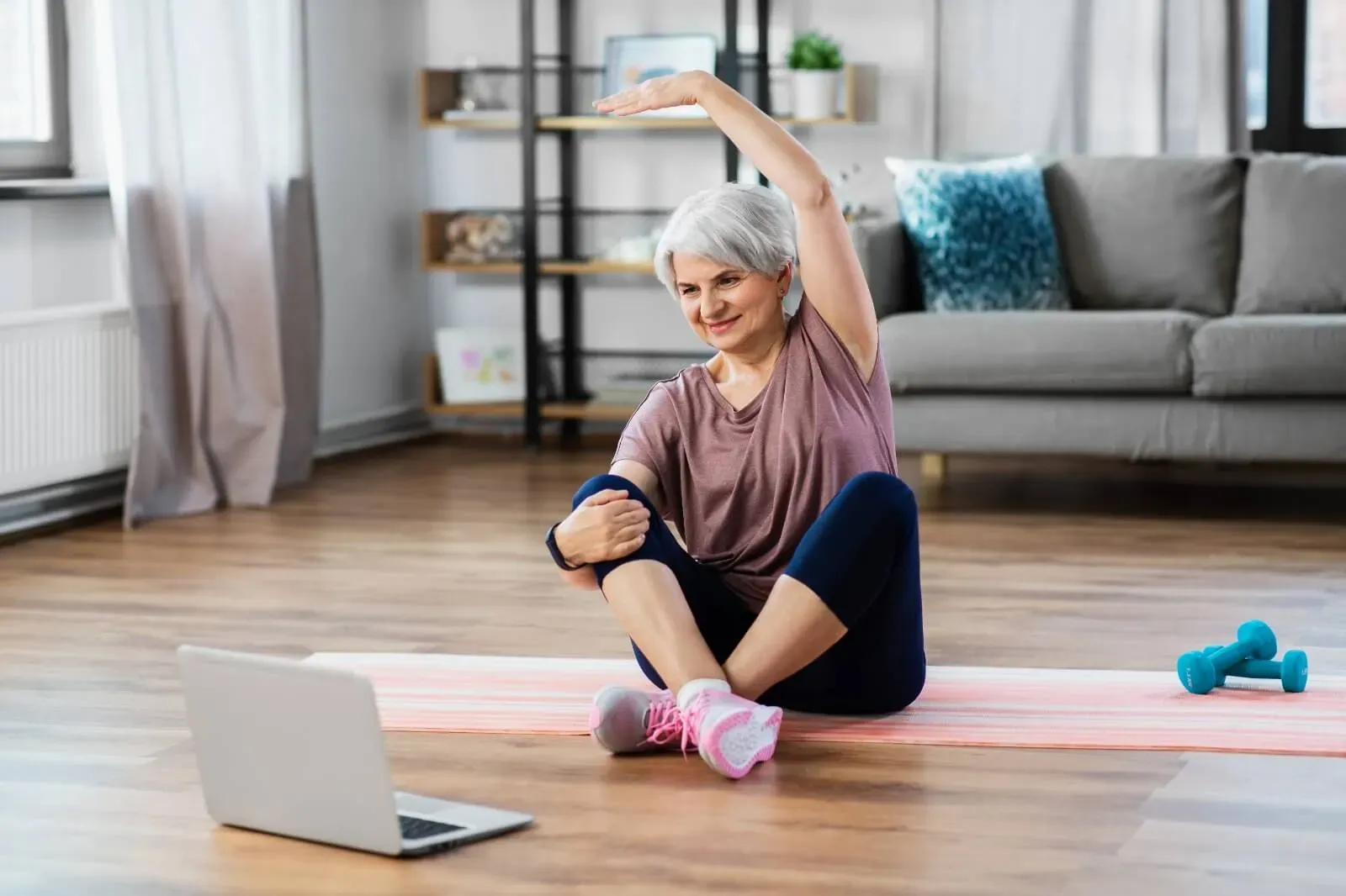 A senior patient doing a guided stretching exercise at home in front of a laptop
